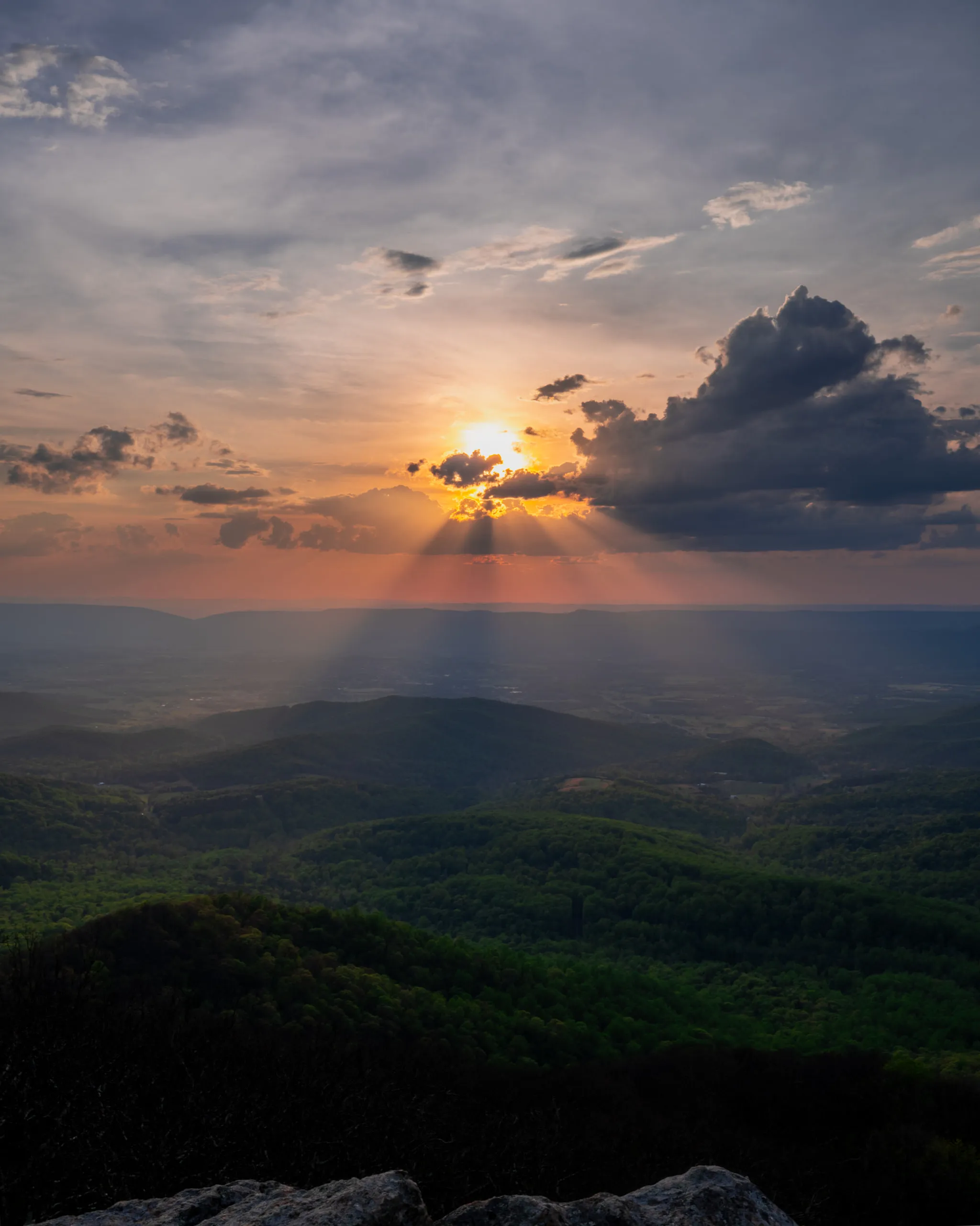 Sunbeams break through cloud over a forested ridge at sunset